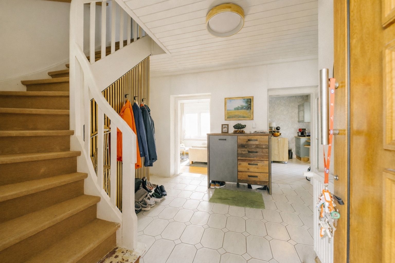 Flur mit Treppe, Garderobe, Schuhen und offener Sicht in angrenzende Räume.