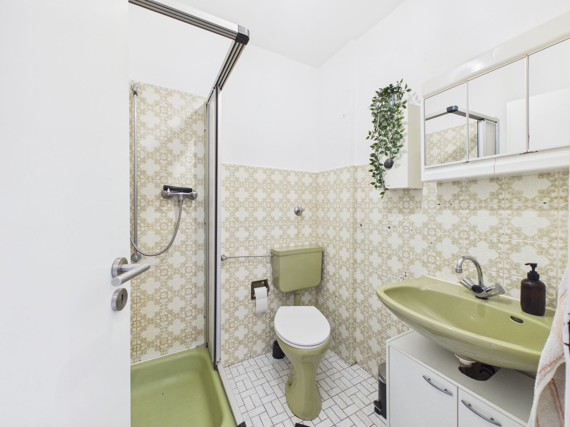 Kleines Badezimmer mit grüner Dusche, Toilette, Waschbecken und Spiegelschrank.