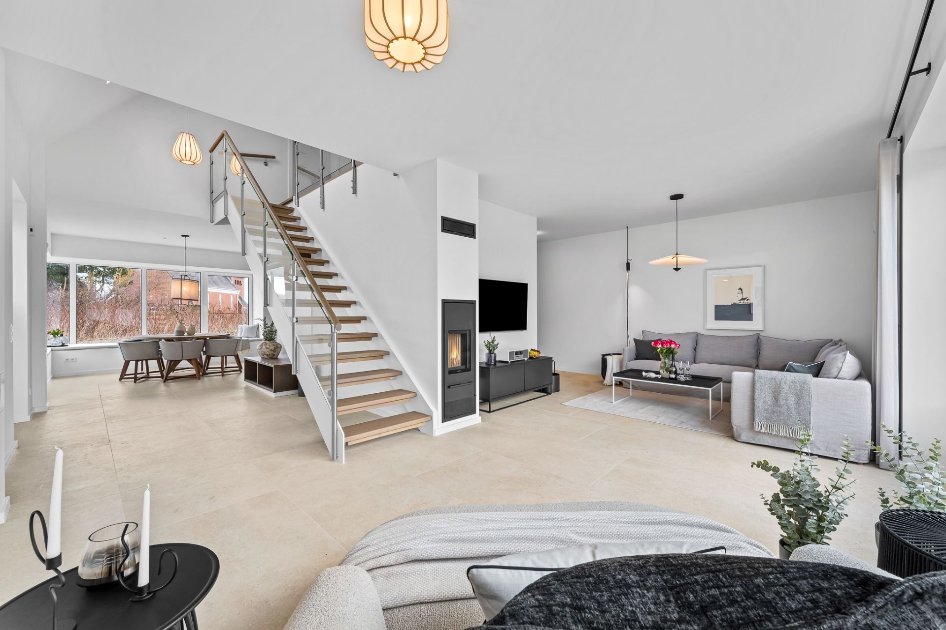 Helles Wohnzimmer mit Treppe, Kamin, Sofa, Fernseher und Esstisch am Fenster.