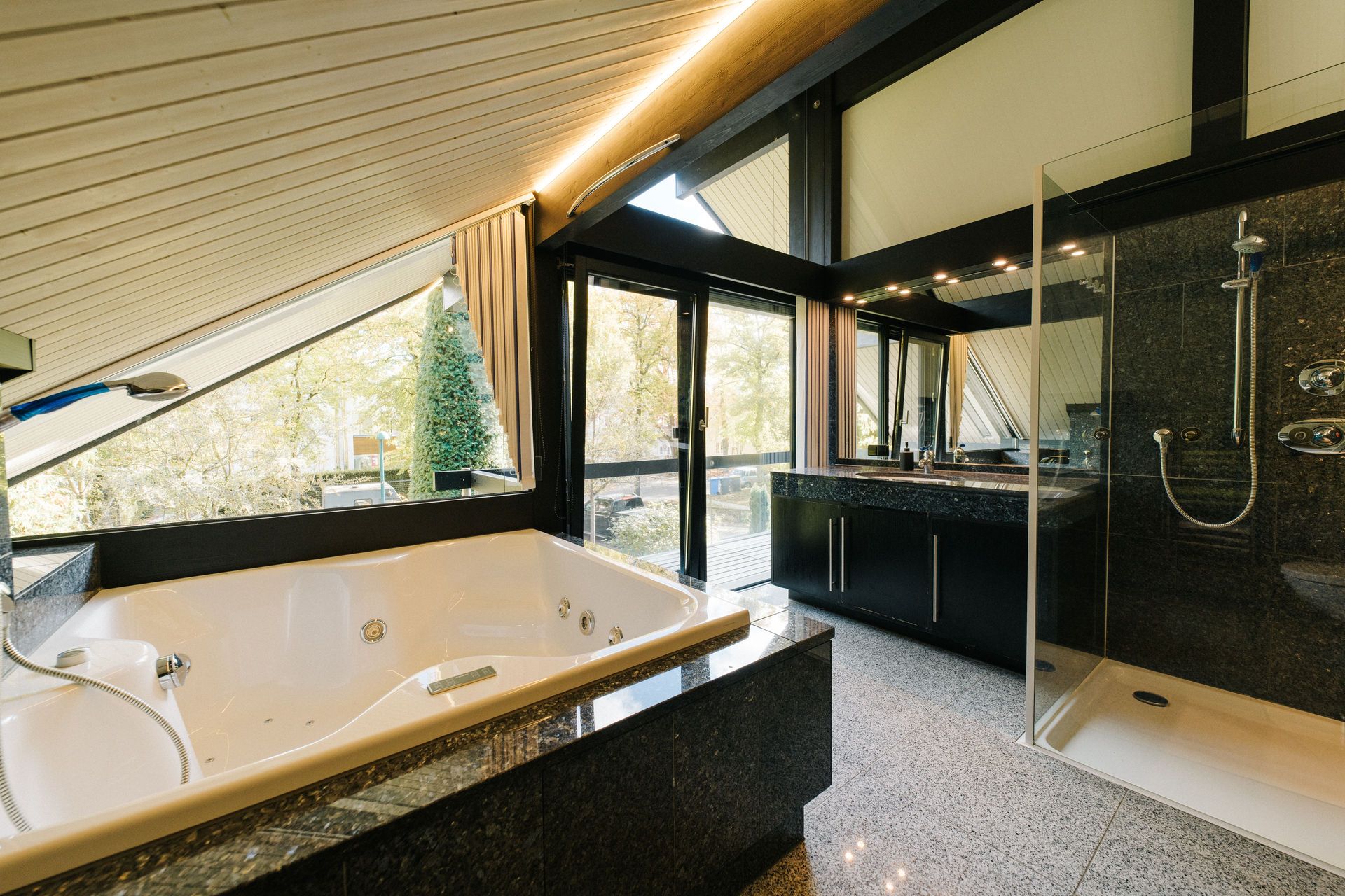 Modernes Badezimmer mit Whirlpool, großer Dusche und breiten Fenstern mit Blick nach draußen.