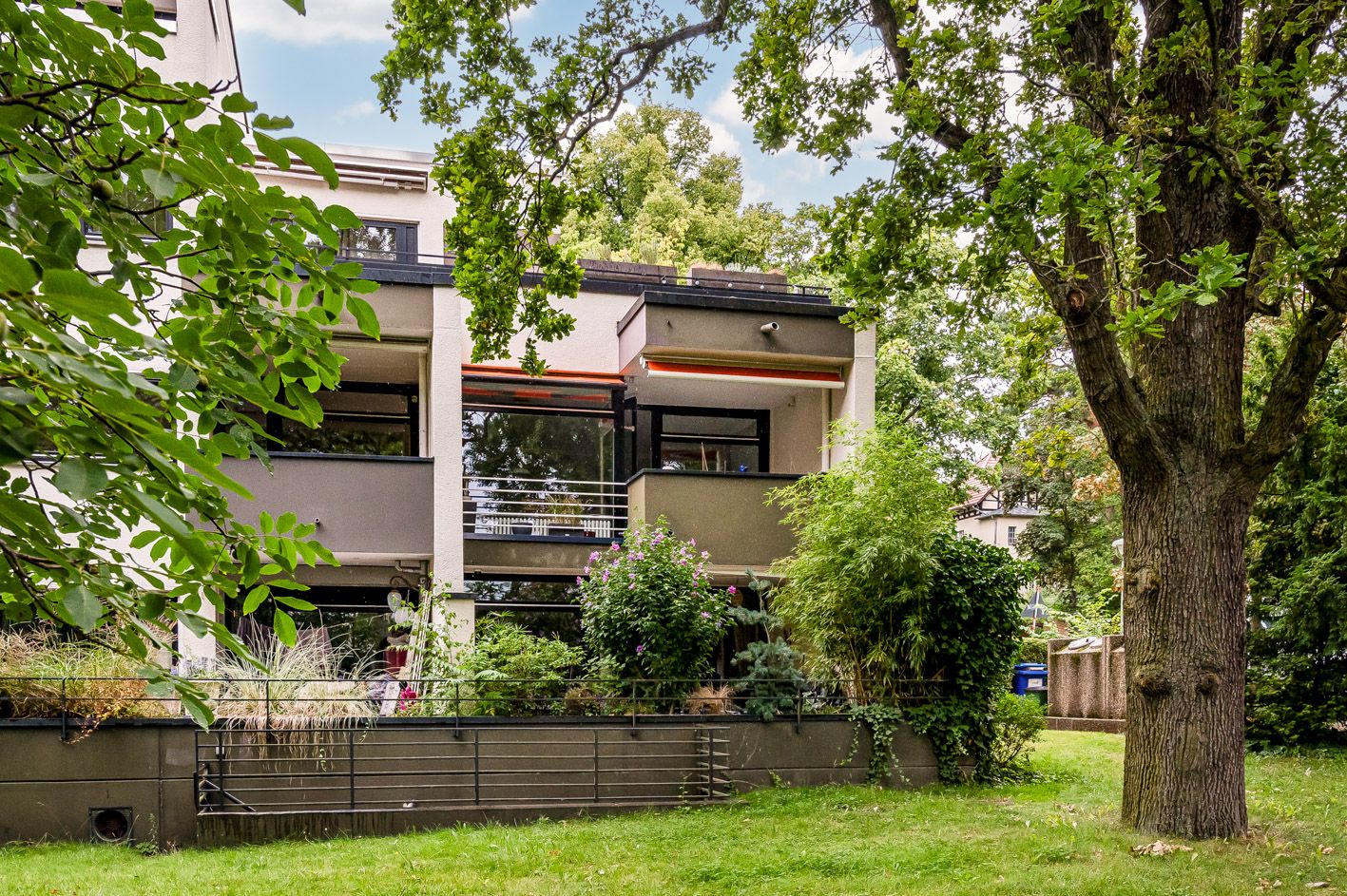 Modernes Wohngebäude mit großen Balkonen und umgeben von Garten und Bäumen.