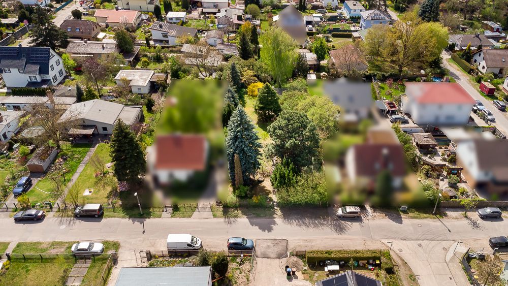 Luftaufnahme von Wohnhäusern mit Gärten, Bäumen und geparkten Autos entlang einer Straße.