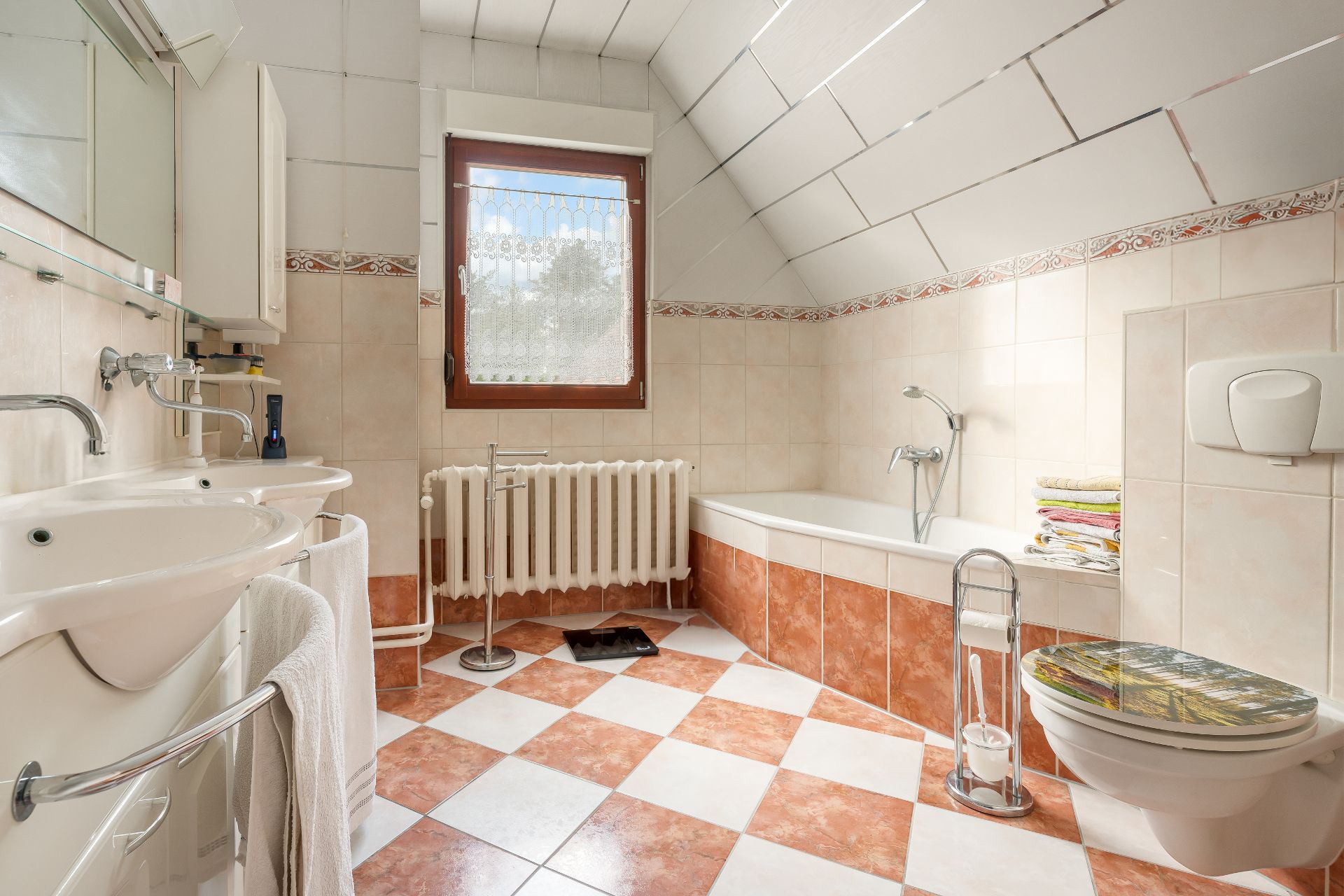 Helles Bad mit zwei Waschbecken, Badewanne, WC, Fenster und gemusterten Fliesen.