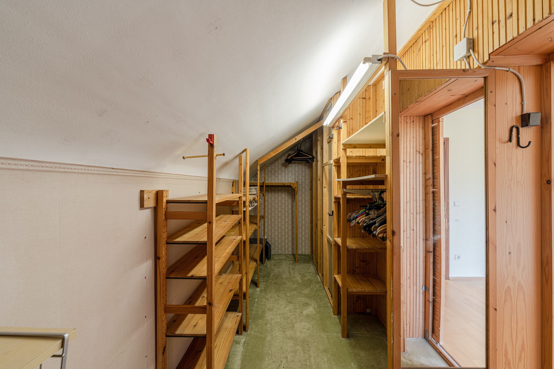 Schmaler begehbarer Kleiderschrank mit Holzregalen und Kleiderstangen unter einer Dachschräge.