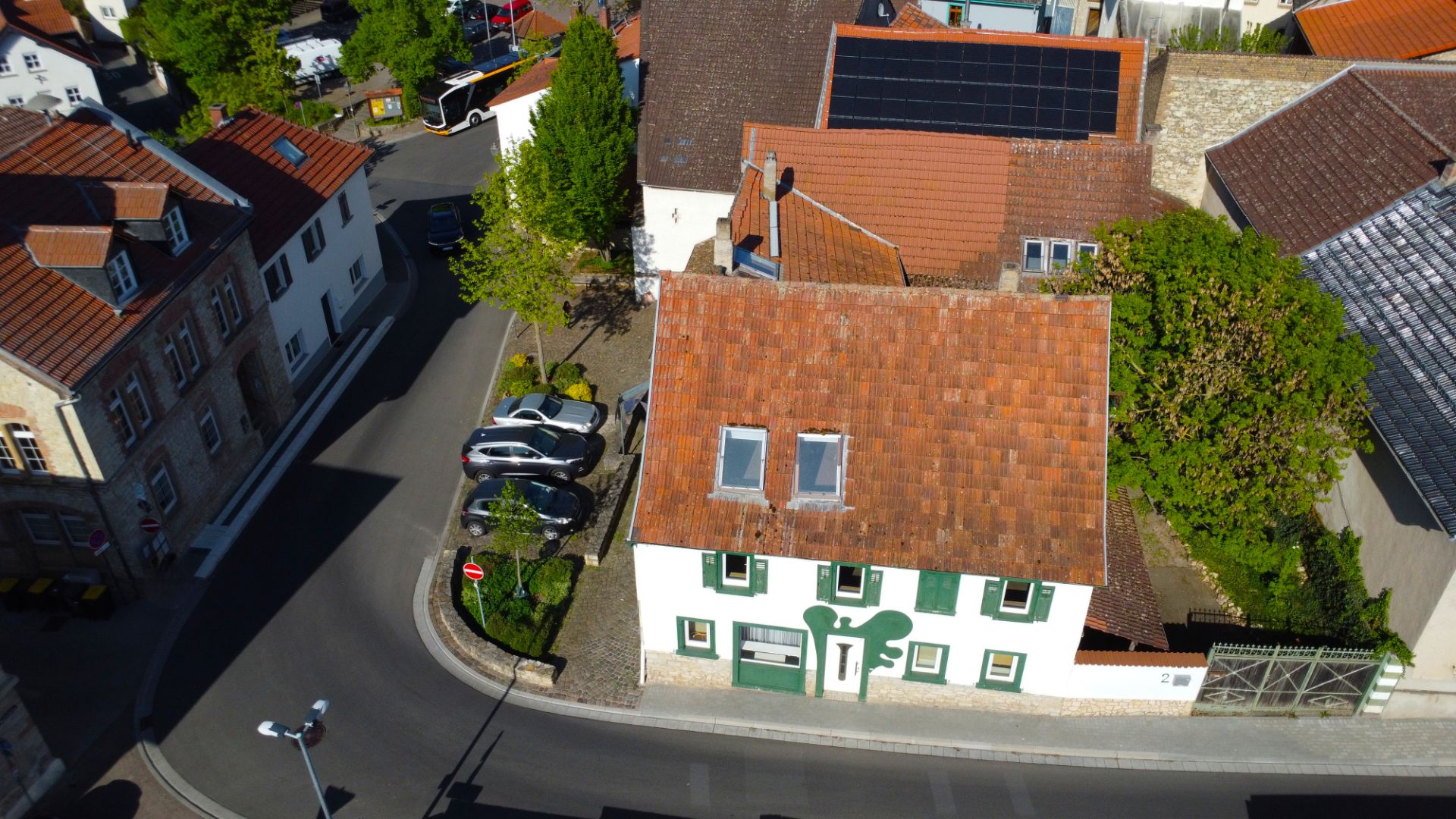 Luftaufnahme eines Wohnhauses mit rotem Dach und mehreren geparkten Autos an einer Straße.