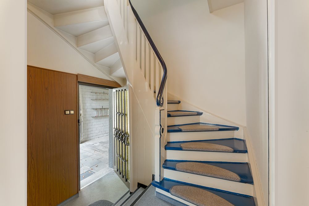 Treppe mit blauem Teppich und offener Tür zu einem gefliesten Raum mit weißen Wänden.