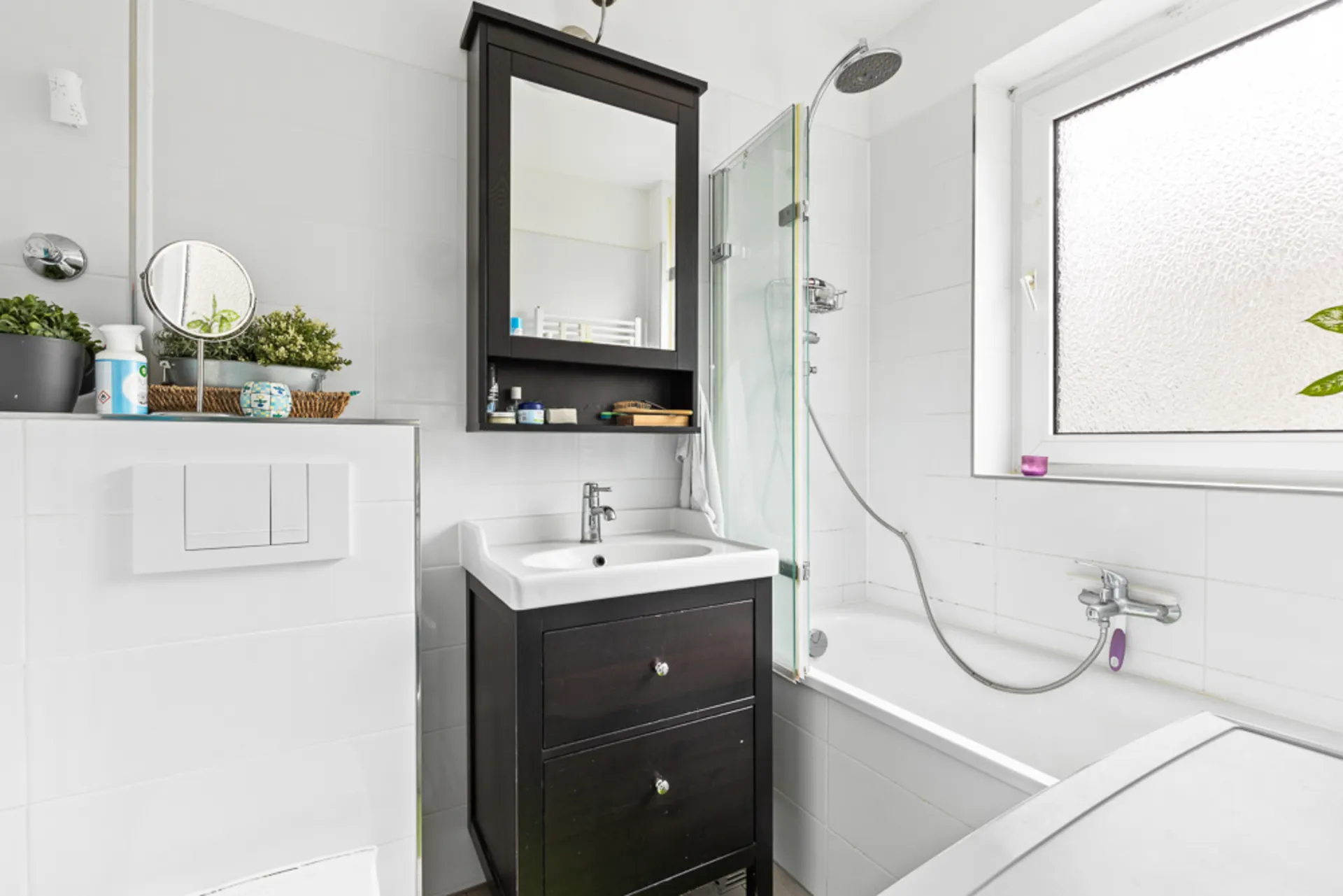 Modernes Badezimmer mit weißer Badewanne, Waschbecken, Spiegel und Pflanzen auf einer Ablage.