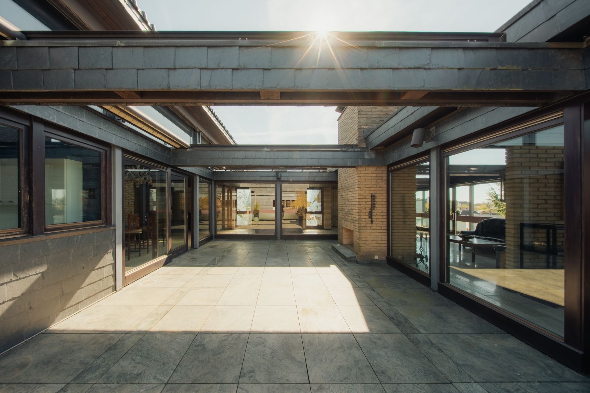 Großer, moderner Innenhof mit Glaswänden und Steinboden, Sonnenlicht scheint durch das Dach.