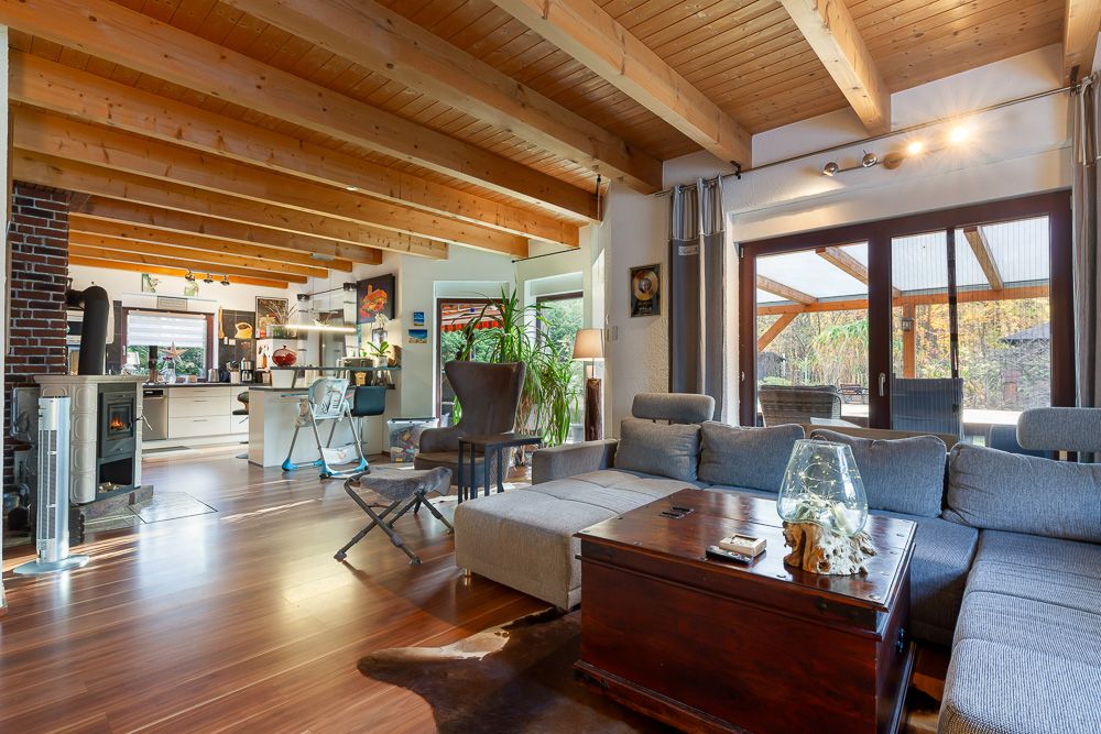 Helles Wohnzimmer mit Holzdecke, Ecksofa, Couchtisch und Zugang zur Terrasse, offene Küche im Hintergrund.