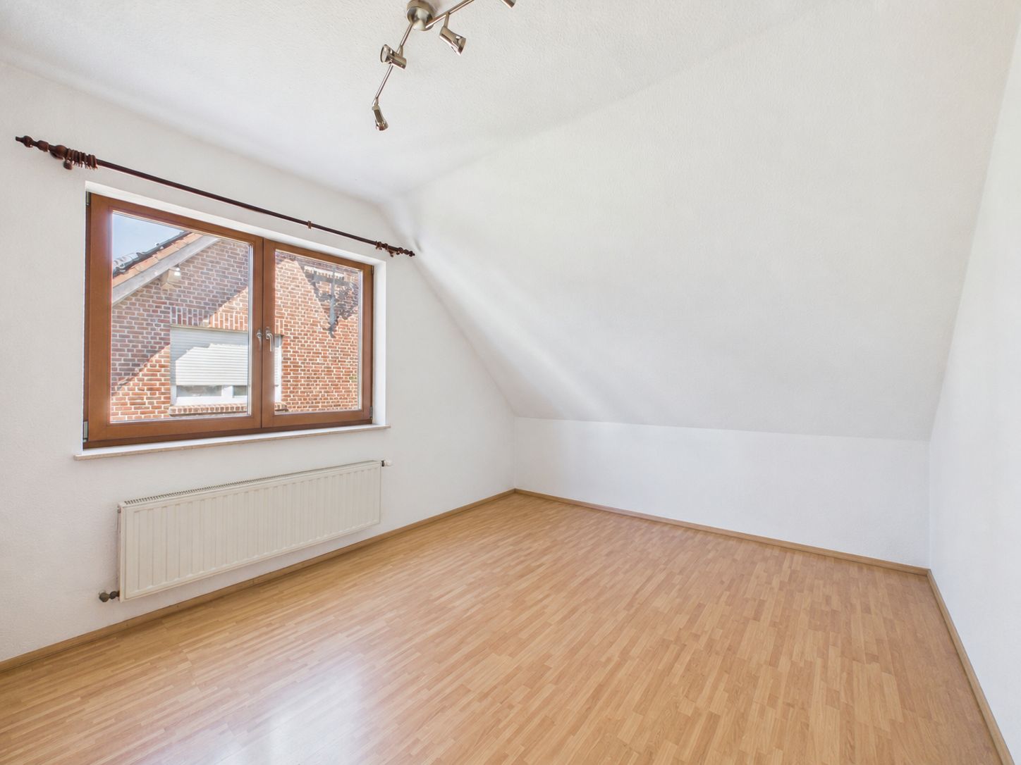 Leerer Raum mit schräger Decke, Holzfußboden und großem Fenster.