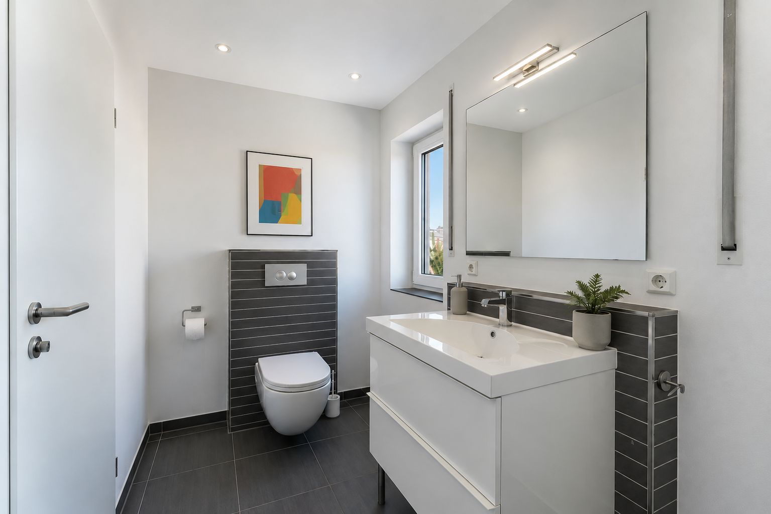 Modernes Badezimmer mit Hänge-WC, weißem Waschbecken, Spiegel und abstraktem Bild an der Wand.