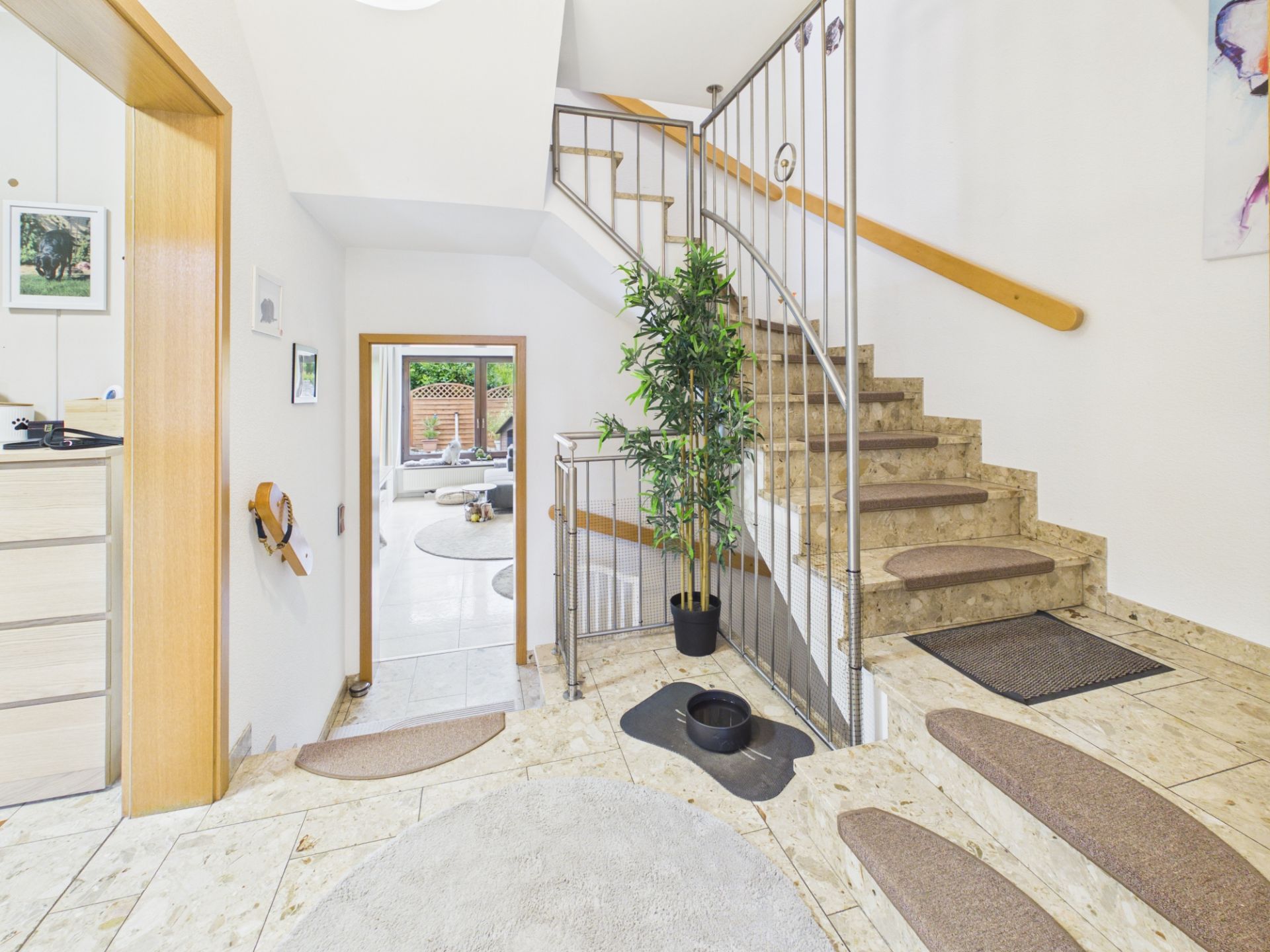 Heller Flur mit Marmortreppe, Pflanze im Topf und Blick auf einen Raum mit Gartenaccessoires.