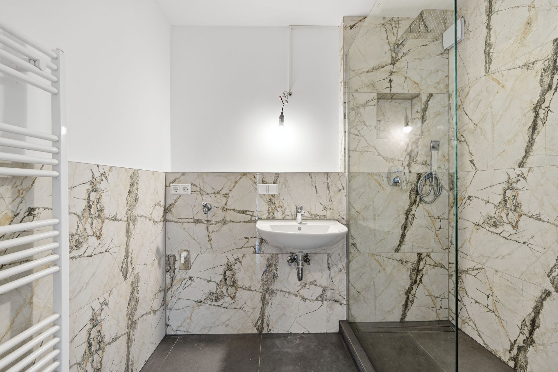 Modernes Bad mit Marmorfliesen, Waschbecken, Glasdusche und Handtuchheizkörper.