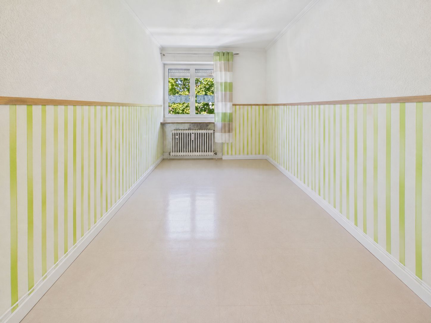 Langer, leerer Raum mit grün-weiß gestreiften Wänden und Fenster mit gestreiftem Vorhang.