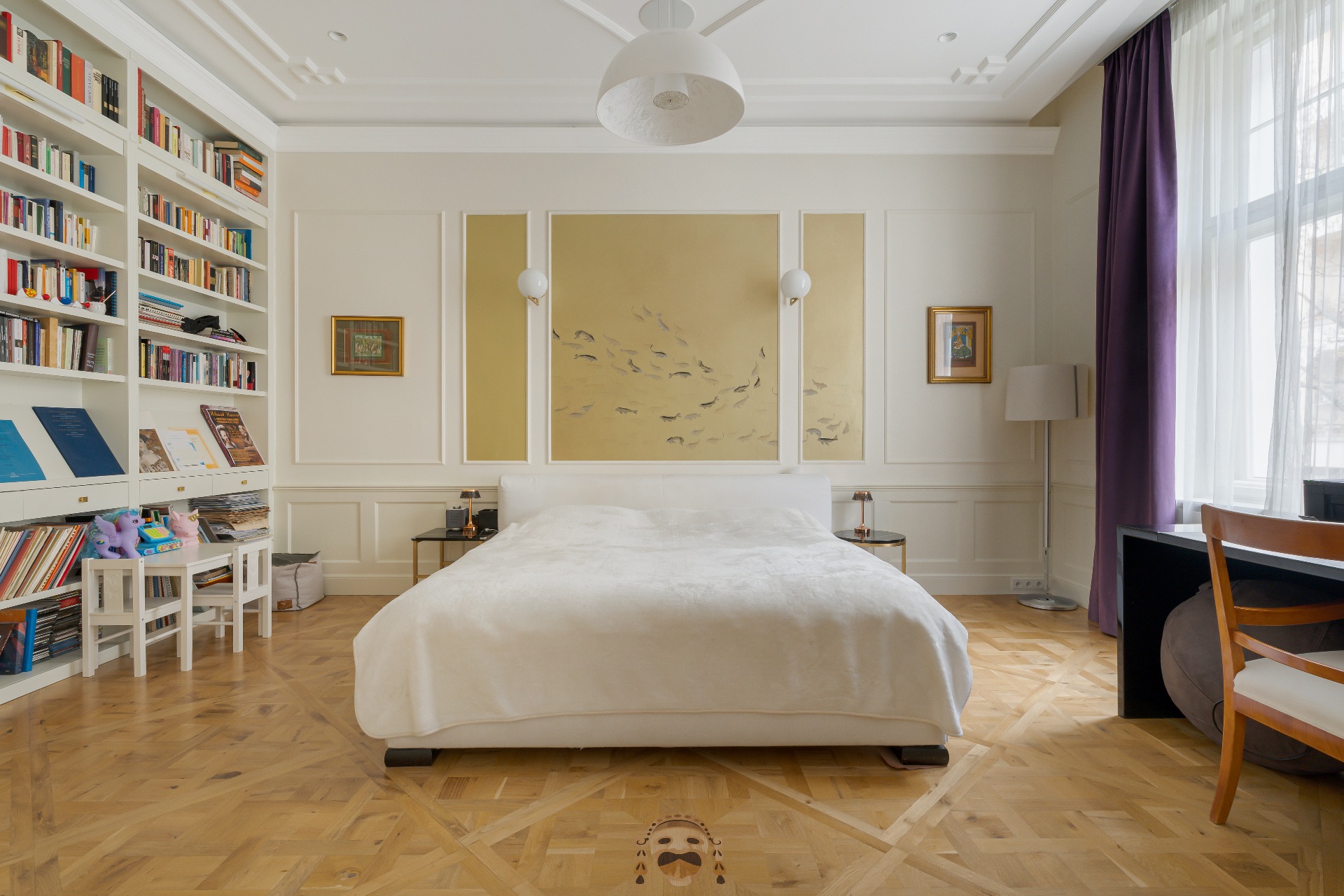 Helles Schlafzimmer mit Doppelbett, Bücherwand, großem Fenster und Schreibtisch mit Stuhl.