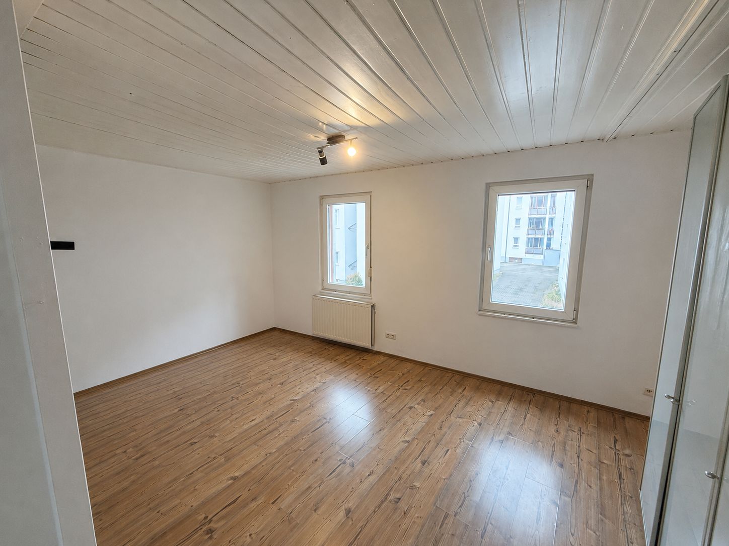 Leerer Raum mit Holzboden, zwei Fenstern, weißer Decke und Wand, Heizung unter Fenster.
