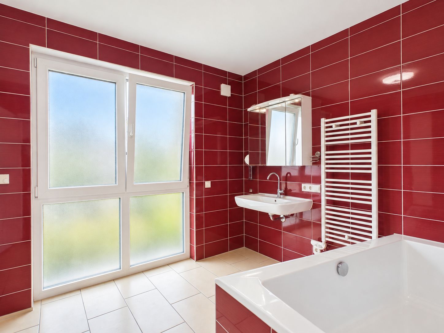 Modernes Bad mit roten Fliesen, großem Fenster, Waschbecken, Spiegel, Handtuchheizkörper und Badewanne.