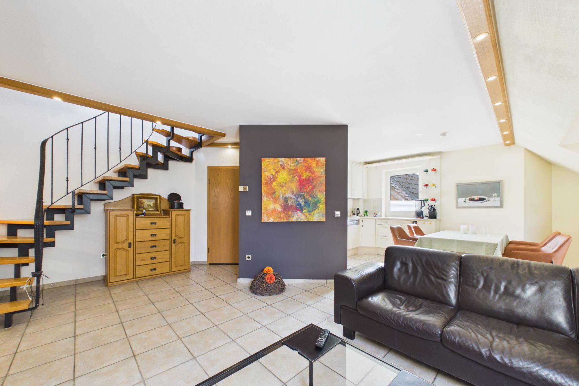 Wohnzimmer mit Ledersofa, offener Treppe, Essbereich und bunter Wandkunst.