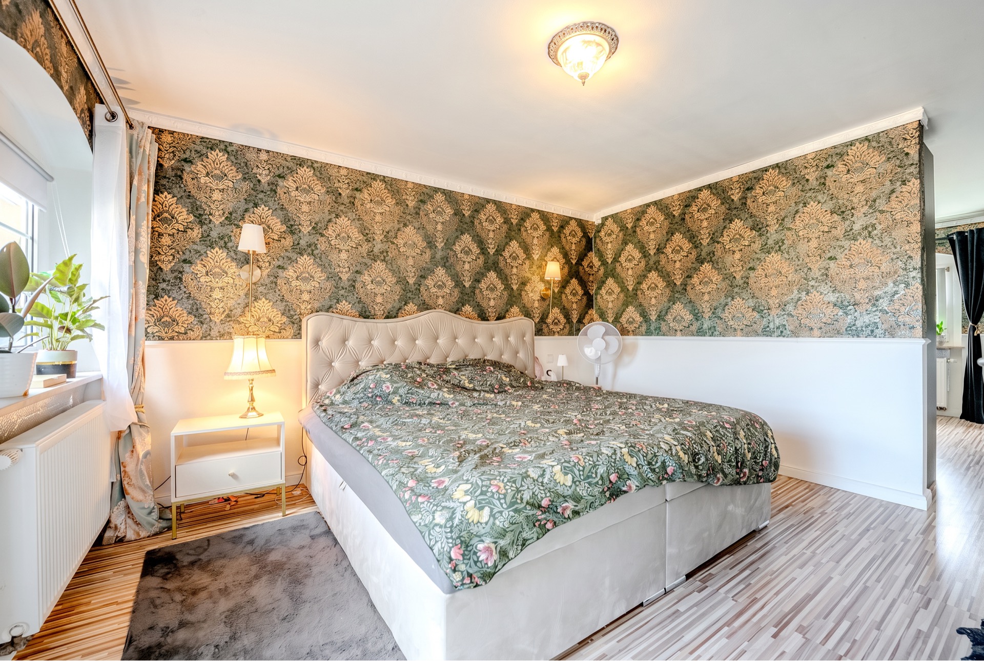Schlafzimmer mit großem Bett, gemusterten Tapeten und zwei Nachttischen mit Lampen.