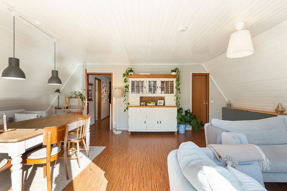 Helles Wohnzimmer mit Holzboden, Esstisch, Sofa und Kommode mit Pflanzen.