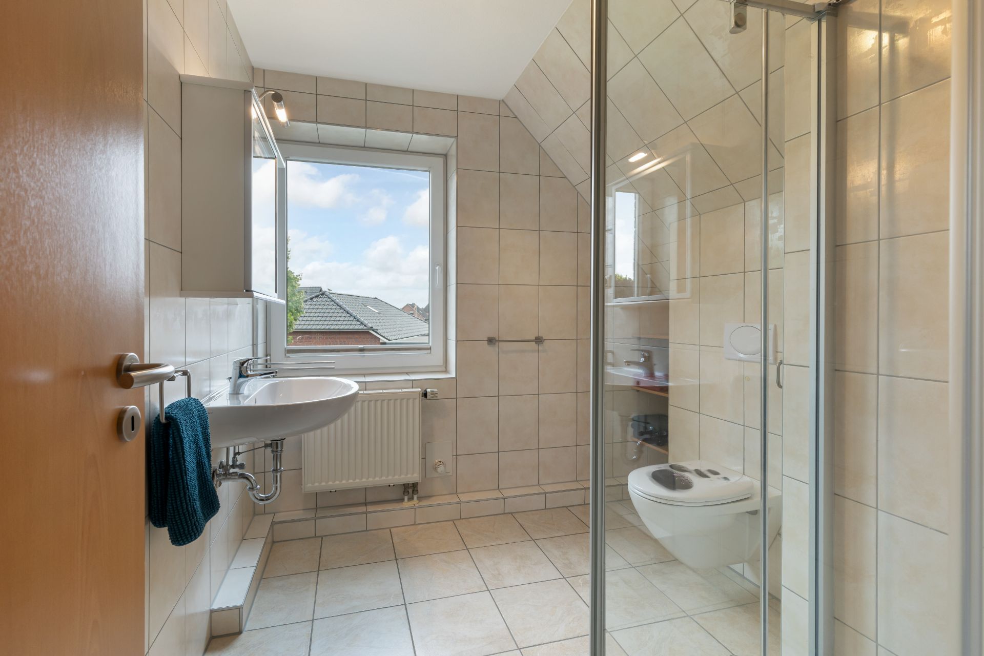 Helles Badezimmer mit Dusche, Waschbecken, WC und Fenster.