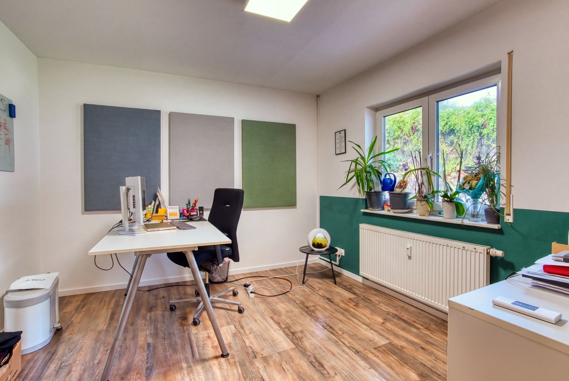 Helles Arbeitszimmer mit Schreibtisch, Bürostuhl, Pflanzen auf der Fensterbank und Holzfußboden.