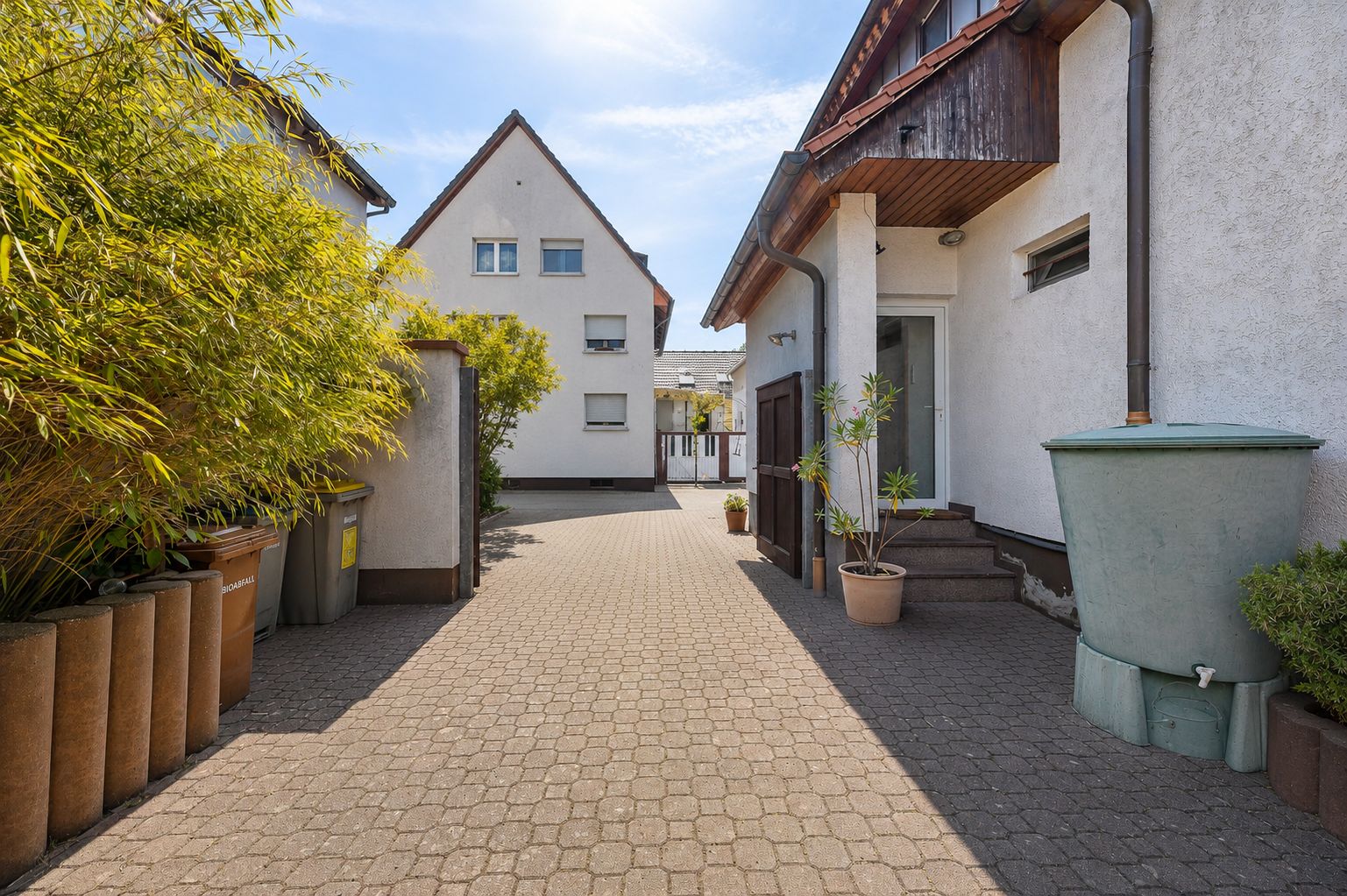 Gepflasterter Hof zwischen weißen Wohnhäusern, mit Pflanzen und Mülltonnen am Rand.