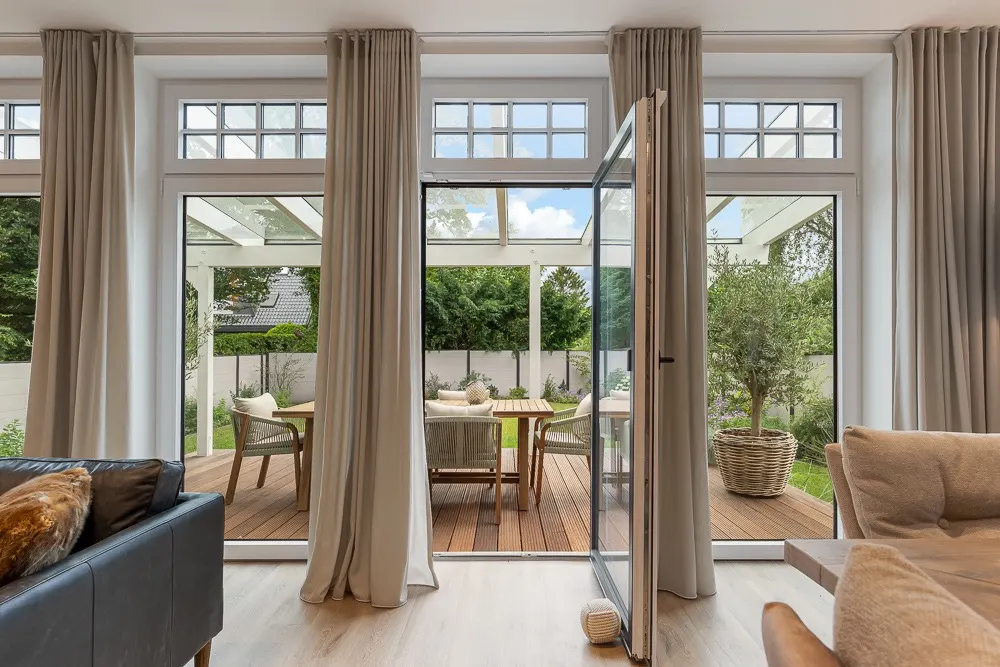 Große Glas-Schiebetür mit Vorhängen, Blick auf Terrasse mit Sitzmöbeln und Garten.