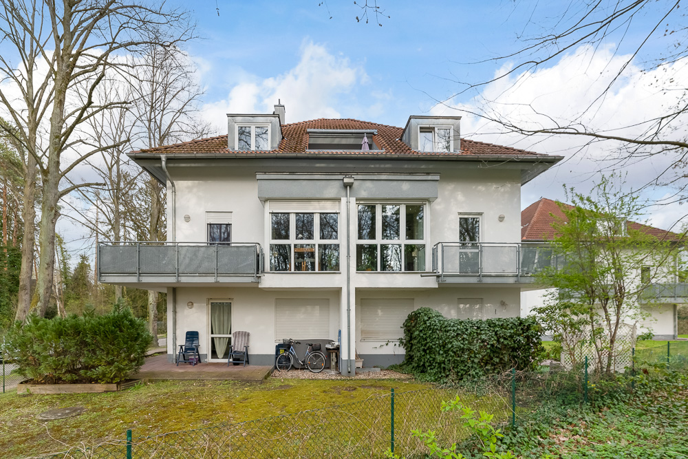 Zweistöckiges Wohnhaus mit Balkon, großen Fenstern und Gartenbereich im Vordergrund.