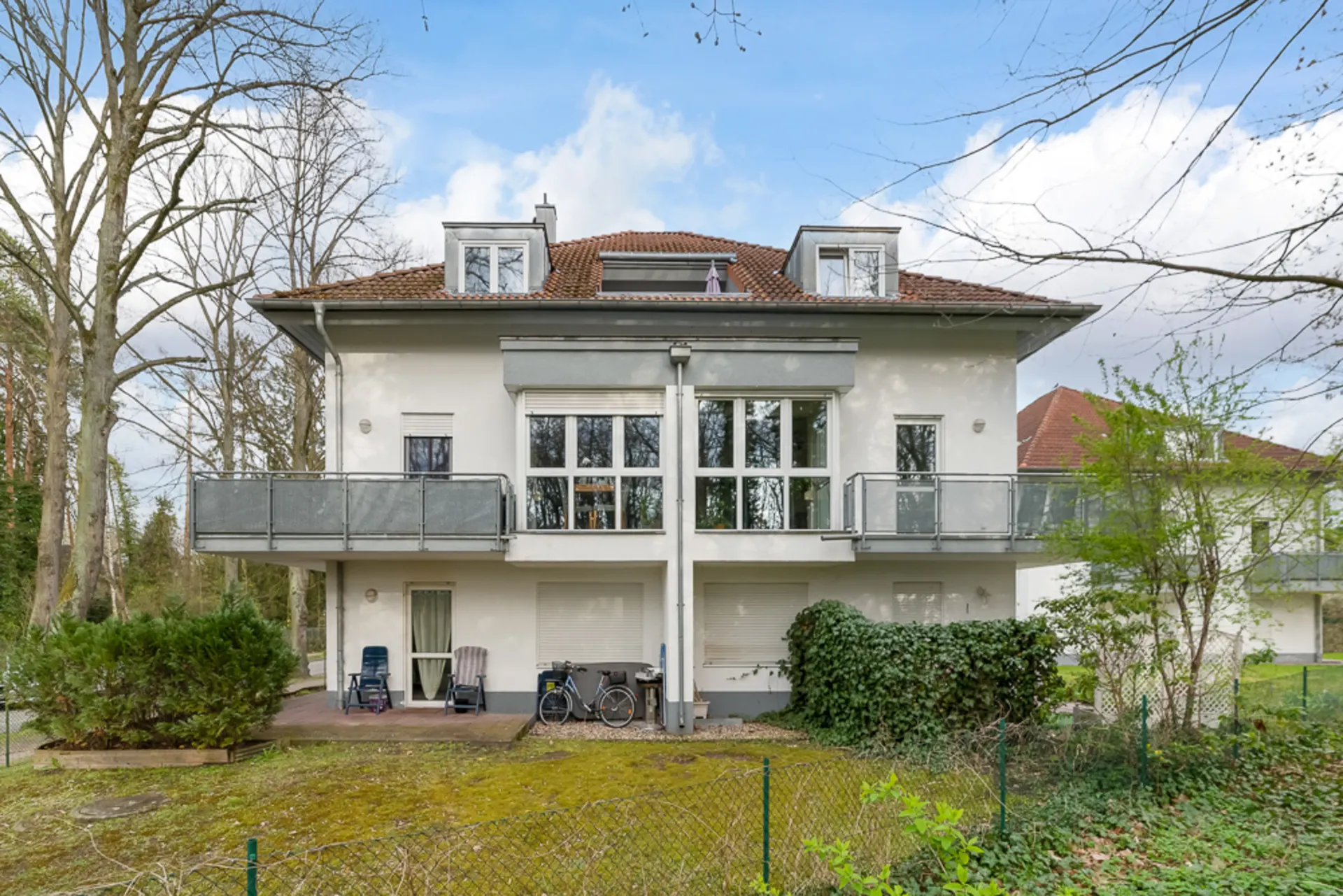 Zweistöckiges Wohnhaus mit Balkon, großen Fenstern und Gartenbereich im Vordergrund.