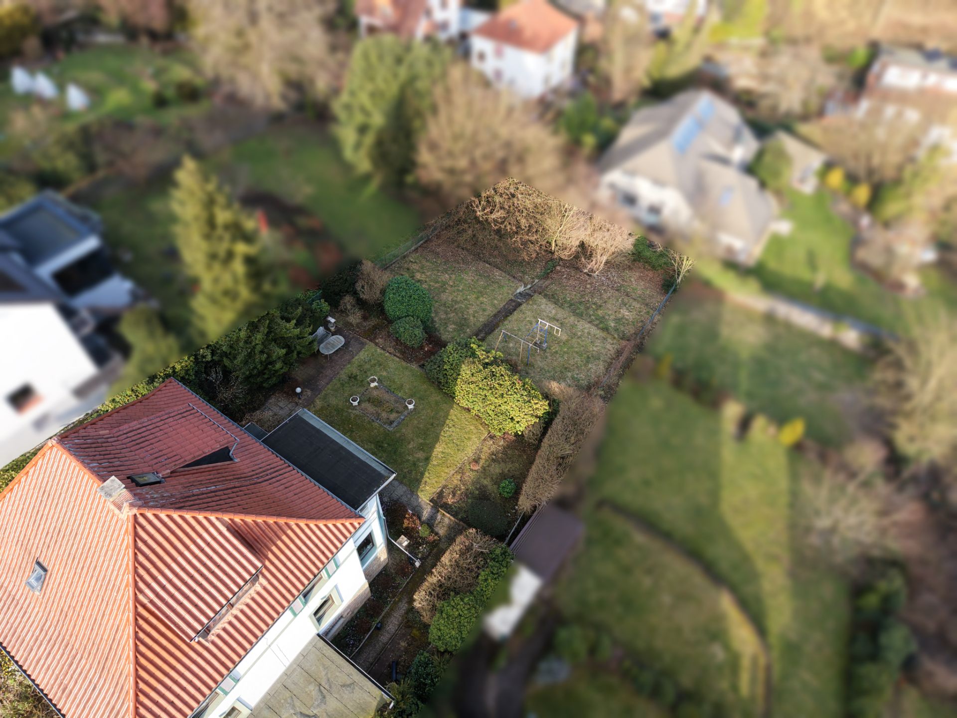 Luftbild eines Hauses mit rotem Dach und großem Garten mit Bäumen und Rasen.