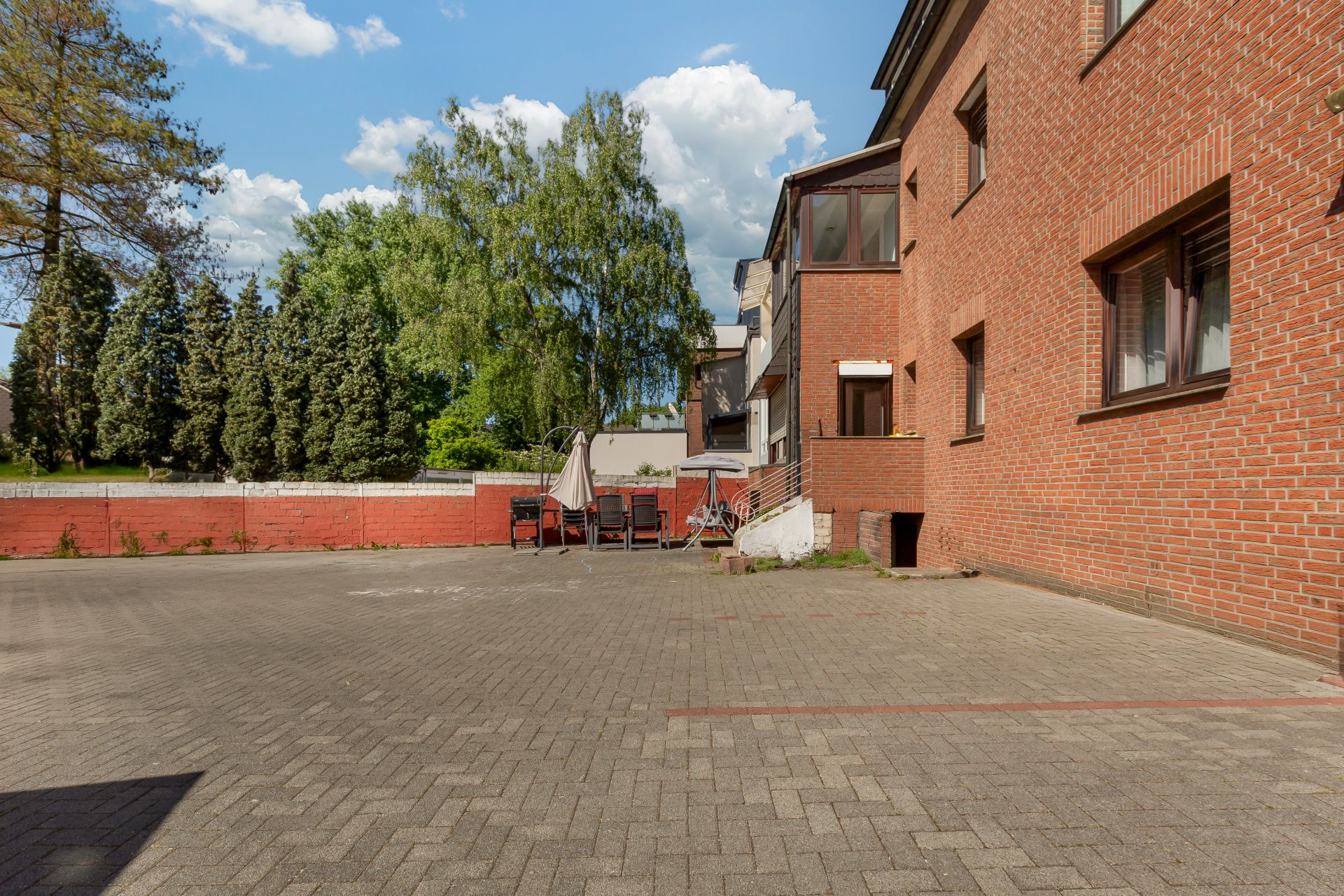 Gepflasterter Hof mit Sitzgruppe und Sonnenschirm an einem roten Backsteingebäude.