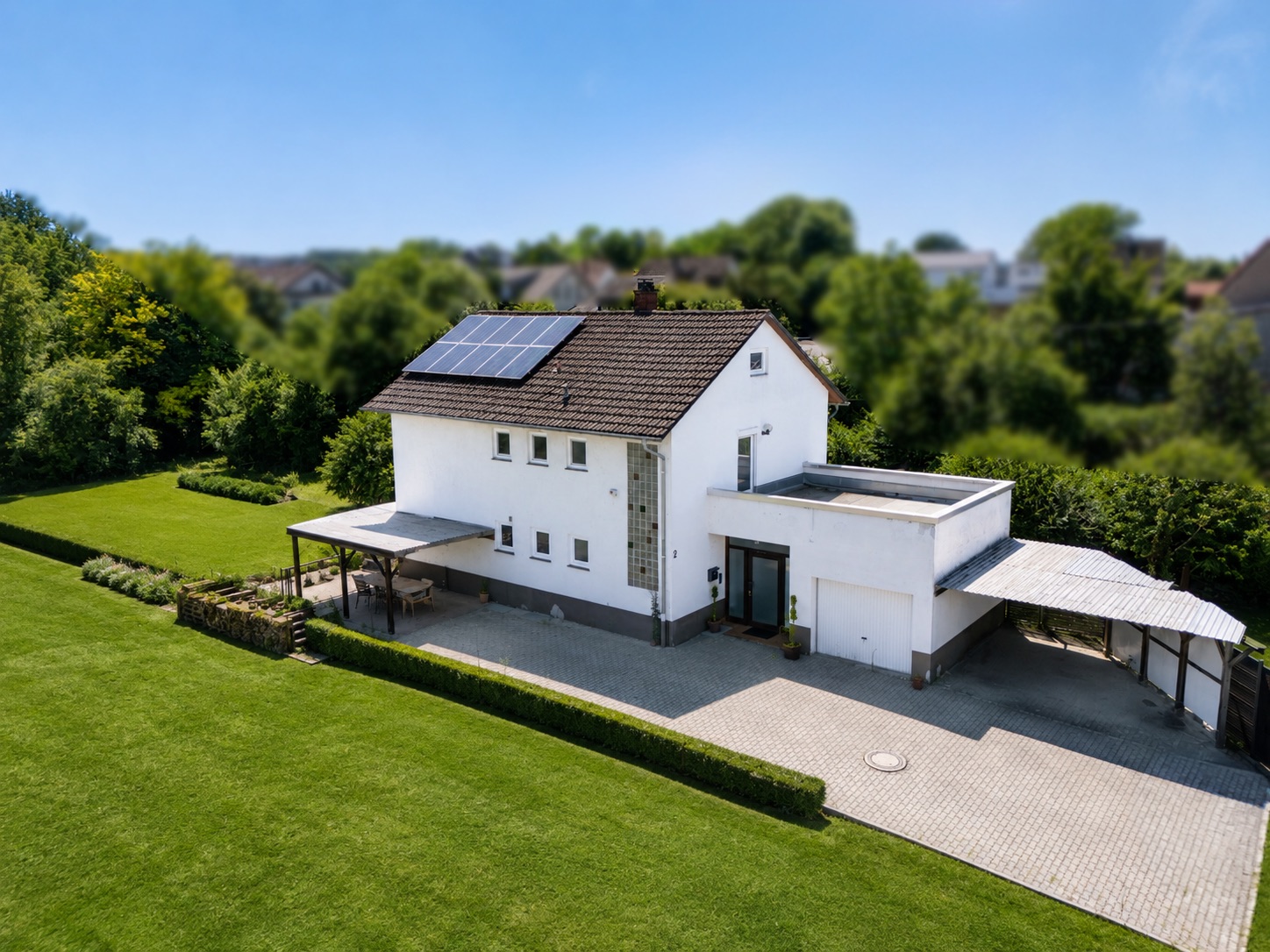 Weißes Einfamilienhaus mit Solarpanelen, Carport und großem gepflegtem Garten.