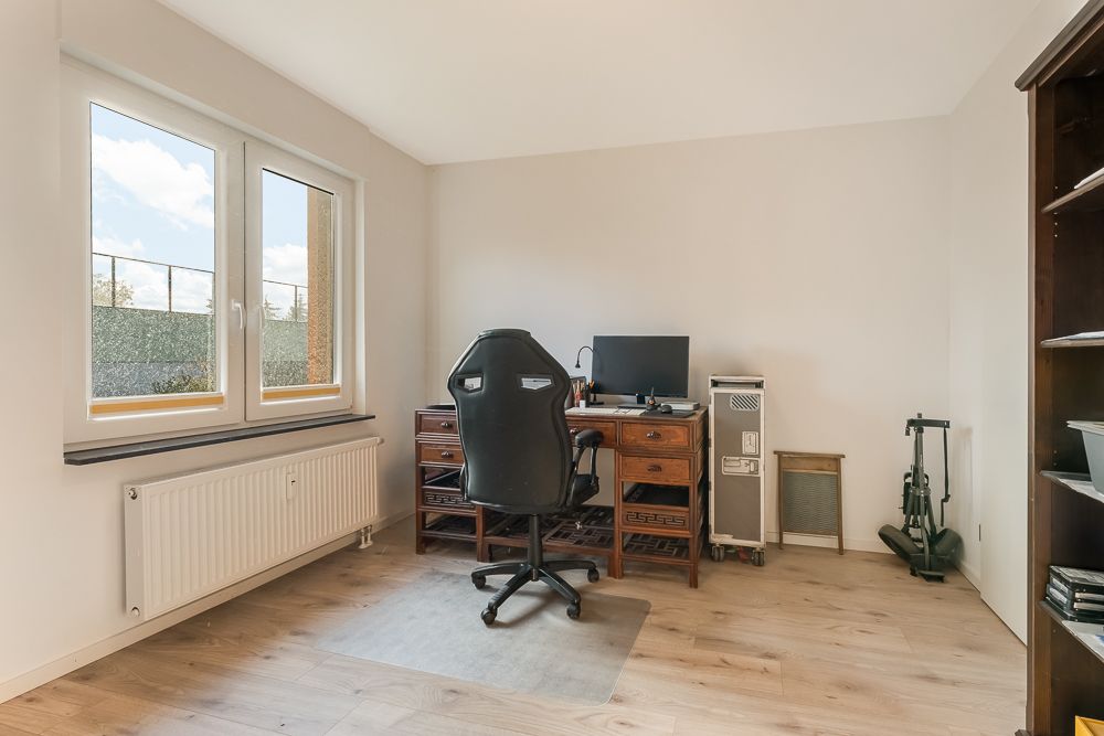 Helles Arbeitszimmer mit Schreibtisch, Bürostuhl, Computer und großem Fenster.