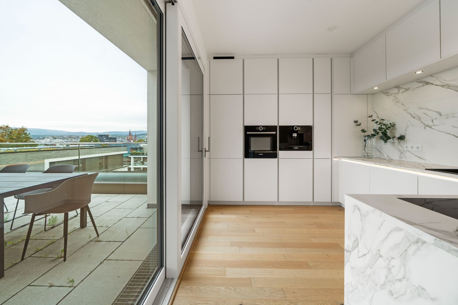 Moderne Küche mit Einbaugeräten und Zugang zur Terrasse mit Sitzbereich.