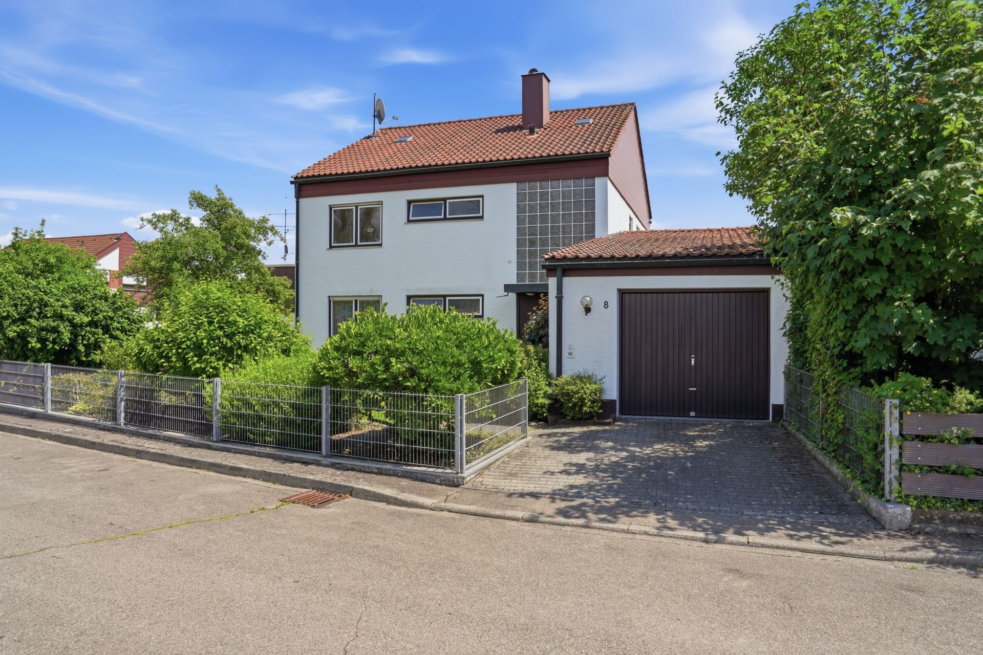 Zweistöckiges Wohnhaus mit Garten, Garage und Metallzaun an einer ruhigen Straße.