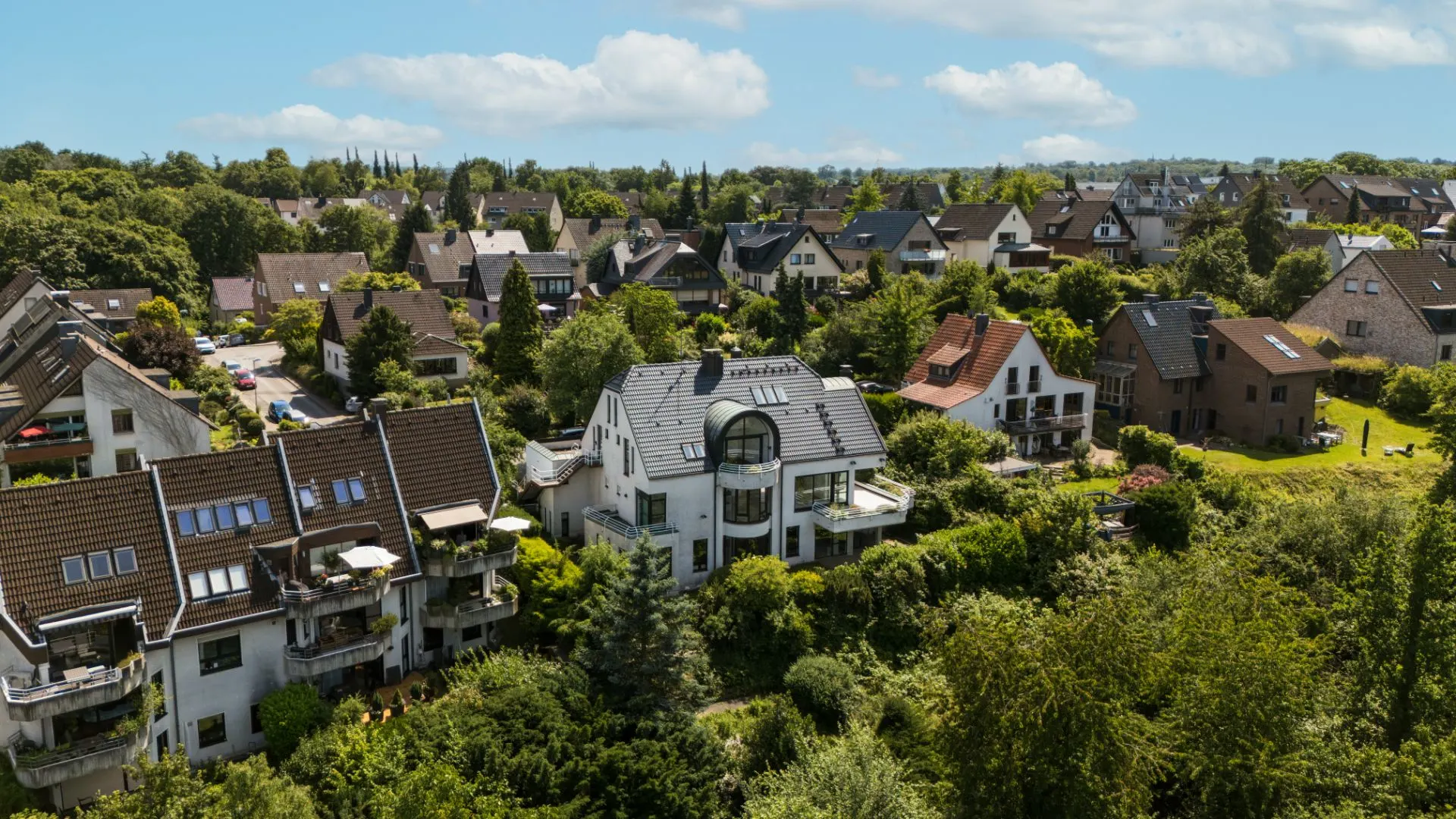 Luftaufnahme von Wohnhäusern mit Gärten und viel Grün in einer ruhigen Wohngegend.