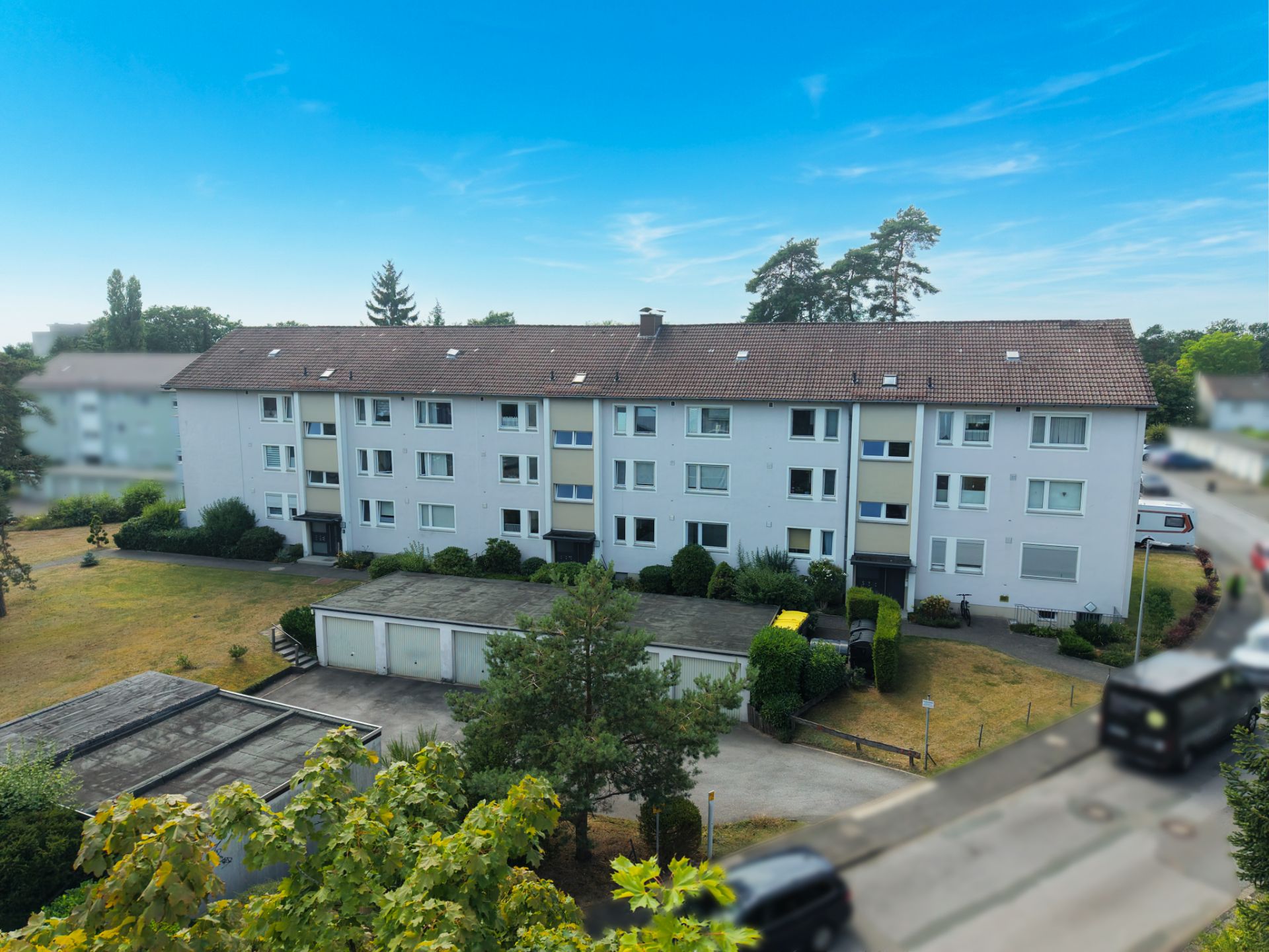Mehrfamilienhaus mit drei Etagen, Garagen und gepflegtem Garten unter blauem Himmel.