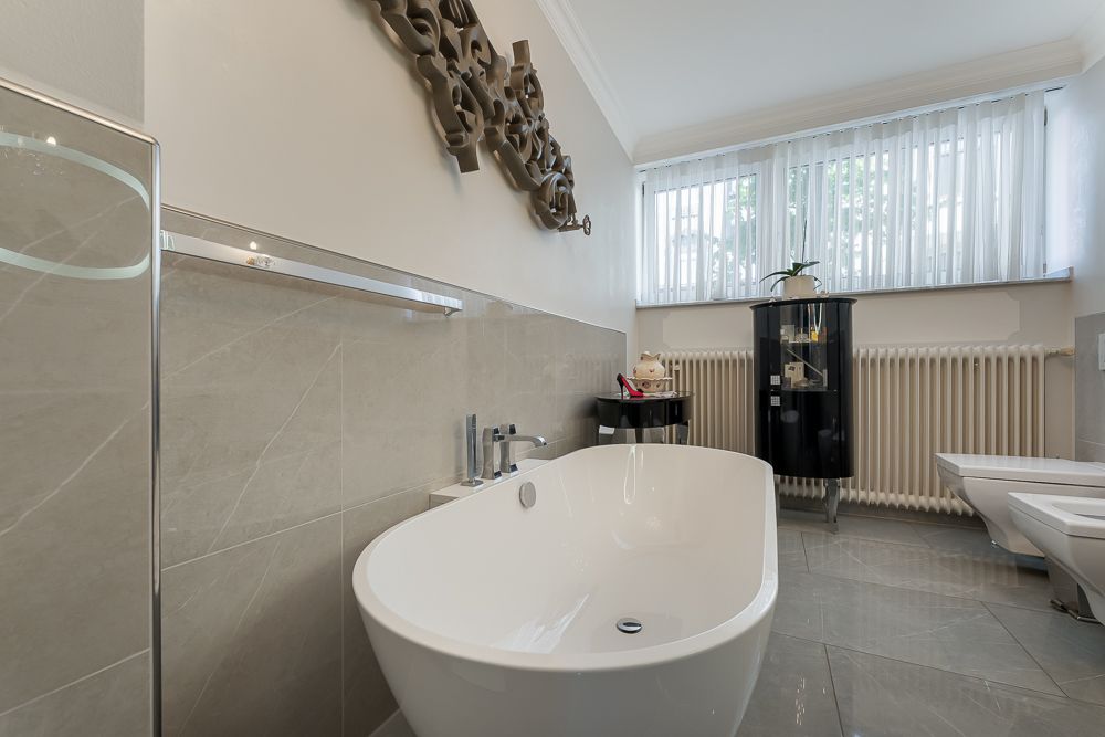 Modernes Badezimmer mit freistehender Badewanne und großem Fenster mit Gardinen.