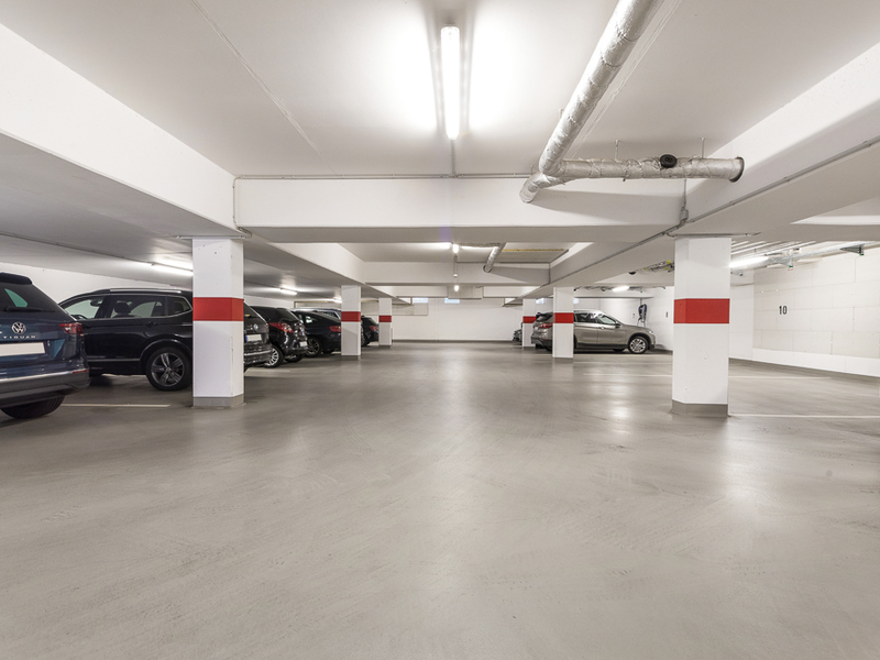 Tiefgarage mit geparkten Autos, weißen Wänden und roten Markierungen an den Pfeilern.