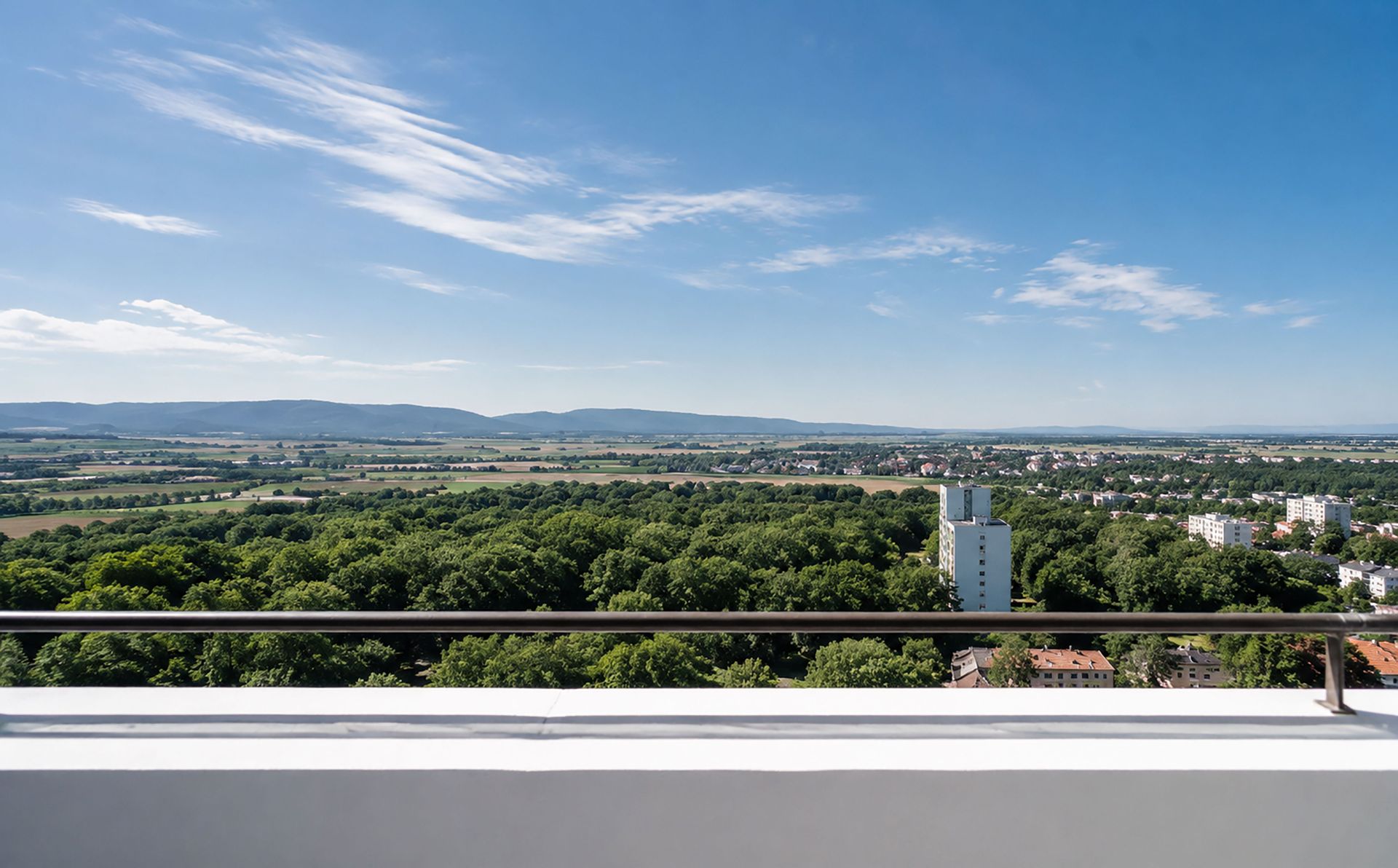 Blick von einem Balkon auf grüne Bäume, Felder und Hügel in der Ferne.