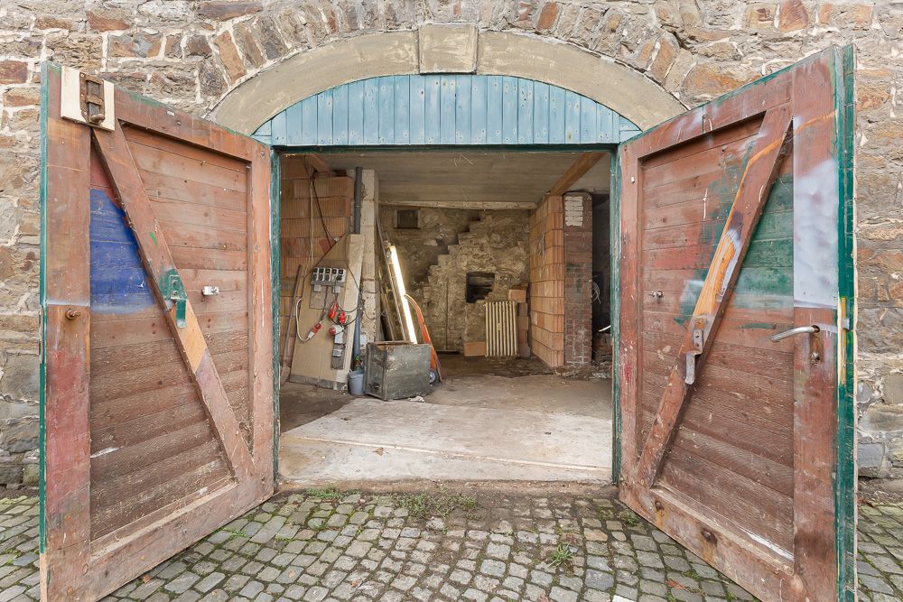 Offene Holztüren führen in eine Werkstatt mit Steinwand und Baumaterialien.