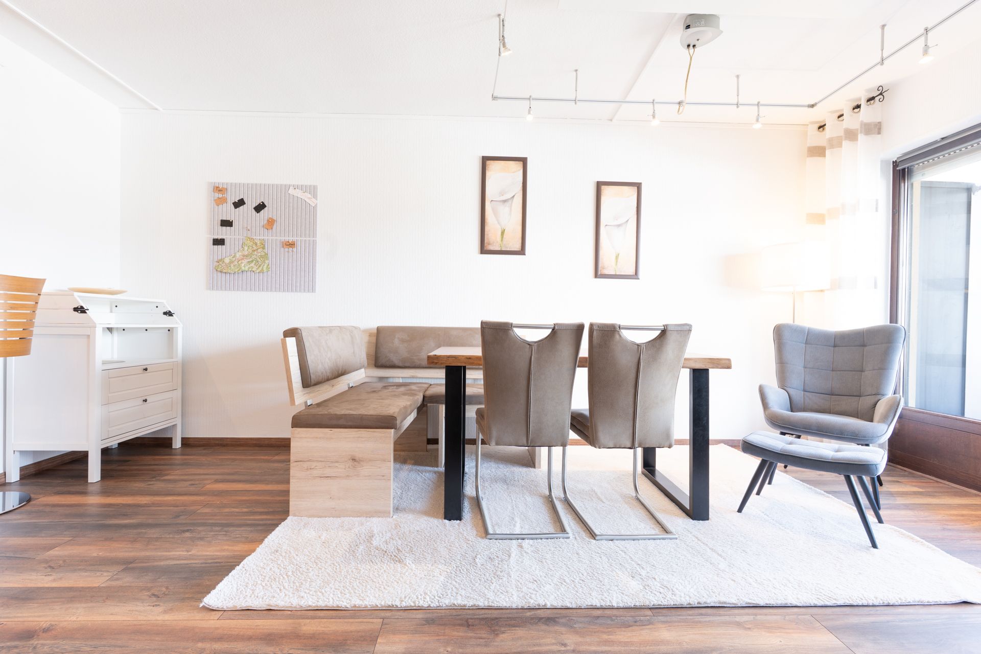 Helles Esszimmer mit Eckbank, Holztisch, vier Stühlen, Sessel und Teppich auf Holzboden.
