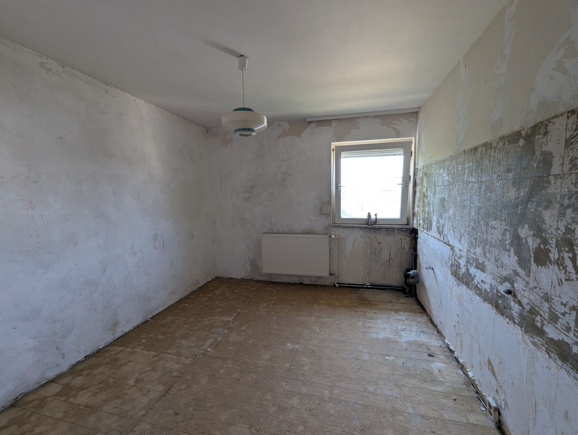Leerer, renovierungsbedürftiger Raum mit Fenster, Heizkörper und abgenutzten Wänden.