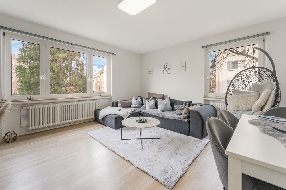 Helles Wohnzimmer mit Ecksofa, Teppich, Couchtisch und großen Fenstern.