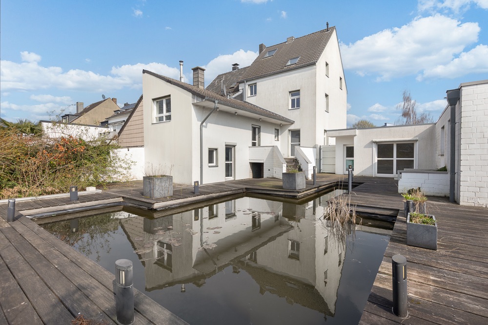 Hinterhof eines Wohnhauses mit Holzterrasse und kleinem Teich.