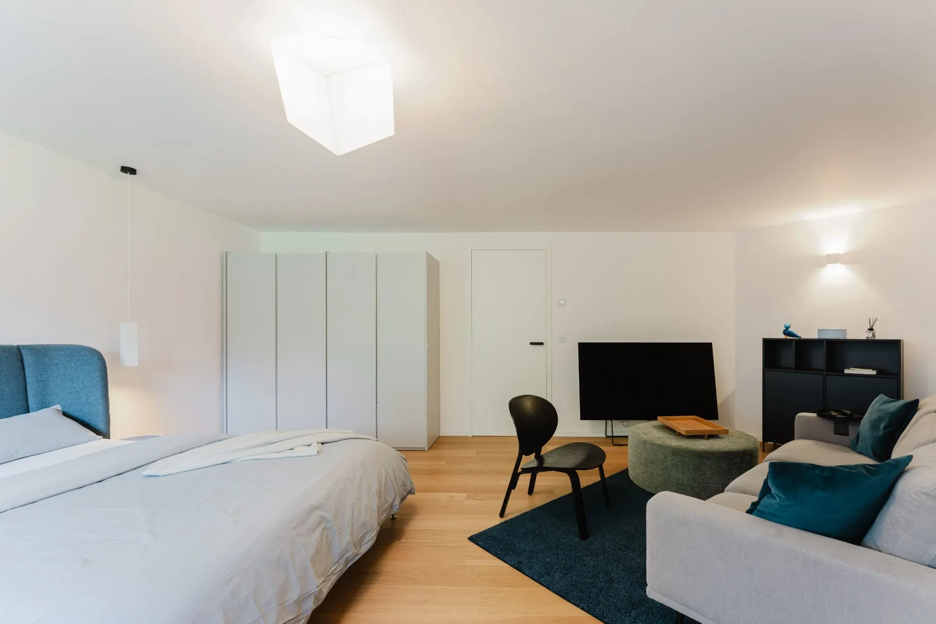 Modernes Schlafzimmer mit Bett, Sofa, Fernseher, Schrank und Stuhl auf Holzfußboden.