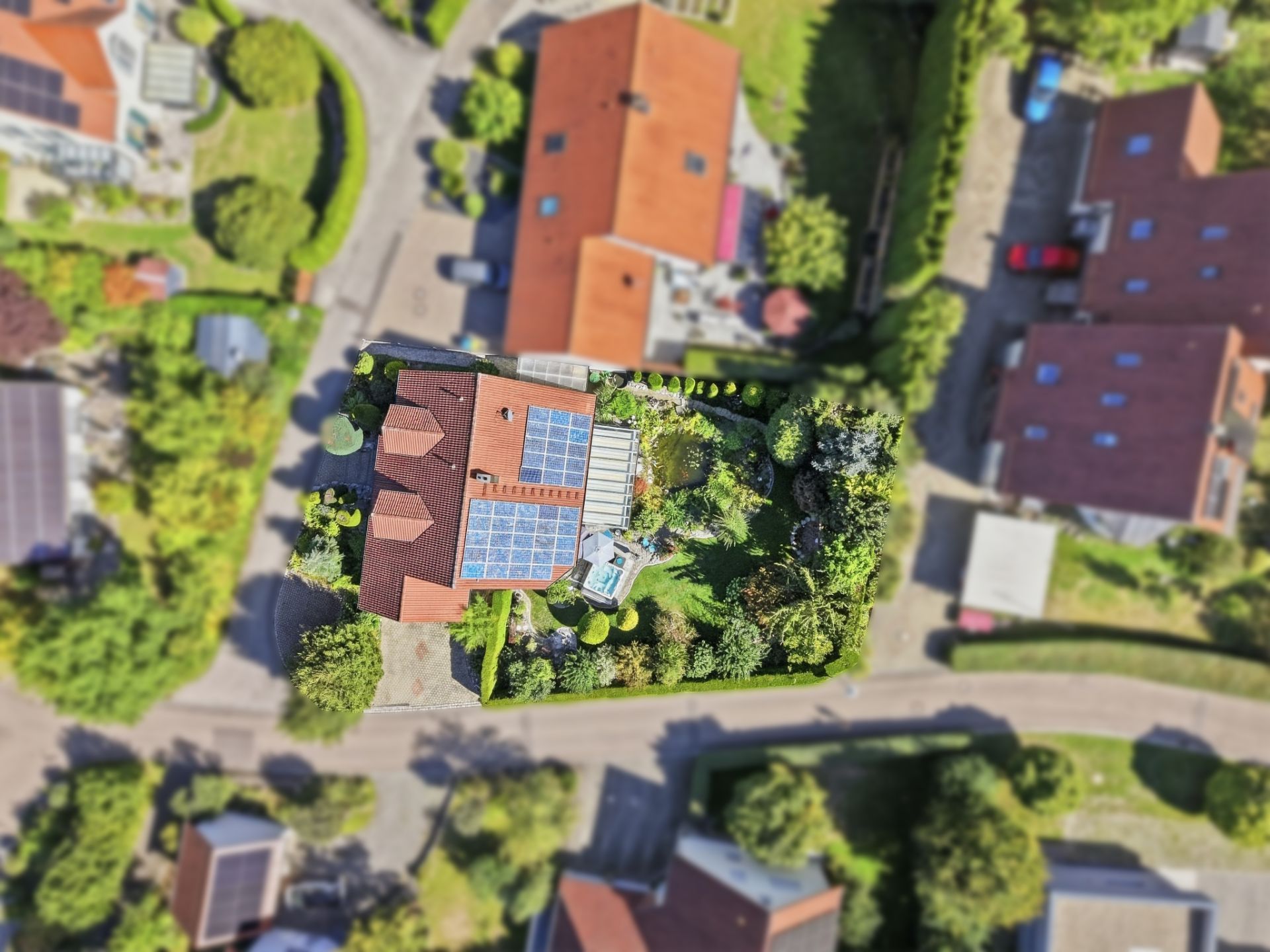 Luftaufnahme eines Hauses mit Solarpanels und großem Garten in einer Wohnsiedlung.