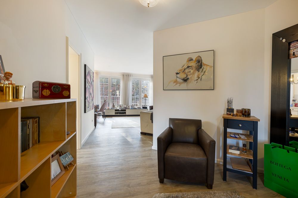 Wohnungsflur mit braunem Sessel, Regal und Blick ins helle Wohnzimmer mit großen Fenstern.