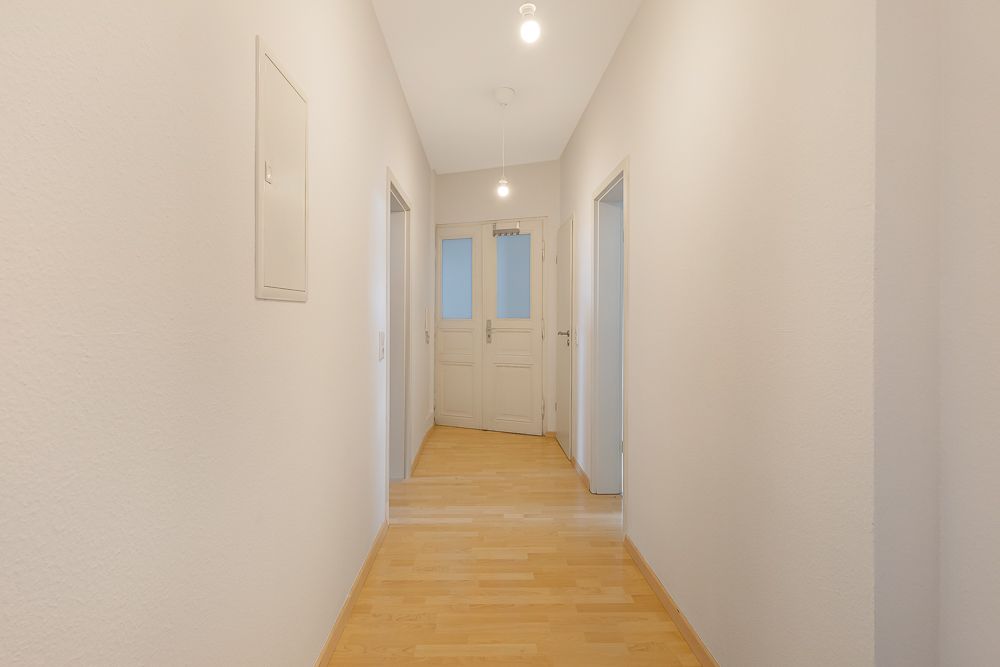 Heller Flur mit Holzboden, weißen Wänden und mehreren Türen zu angrenzenden Räumen.